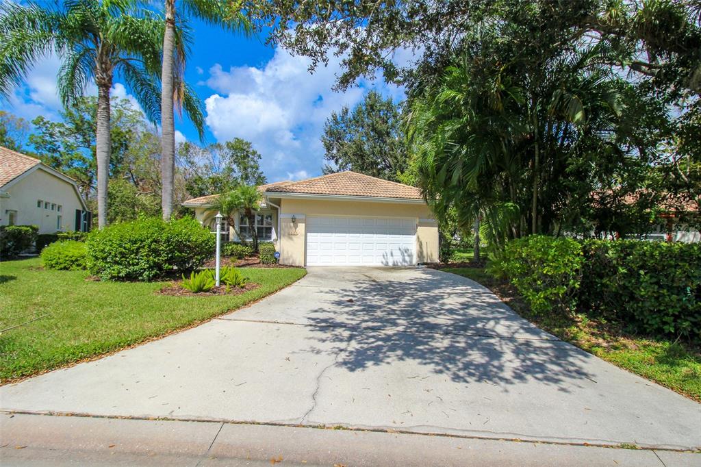 A single-story house with a white garage door, a concrete driveway, and surrounding palm trees — 6662 OAKBROOKE CIRCLE, BRADENTON, FL