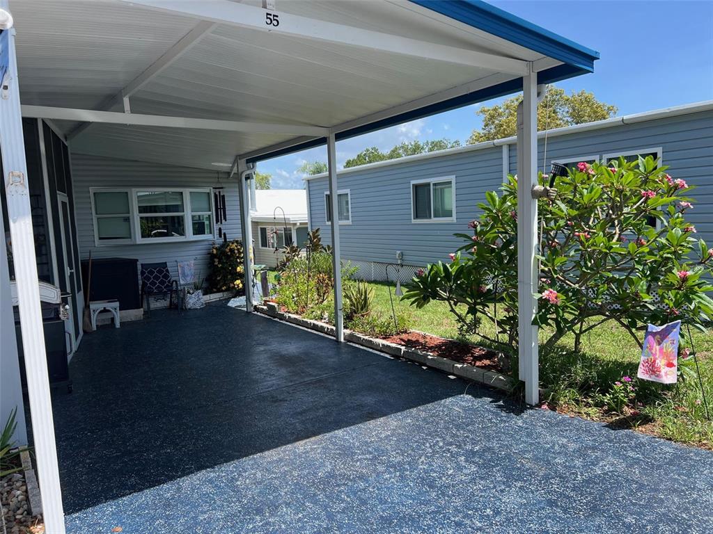 A covered carport with a dark speckled floor sits beside a light blue mobile home — 55 PALM FOREST DRIVE, LARGO, FL