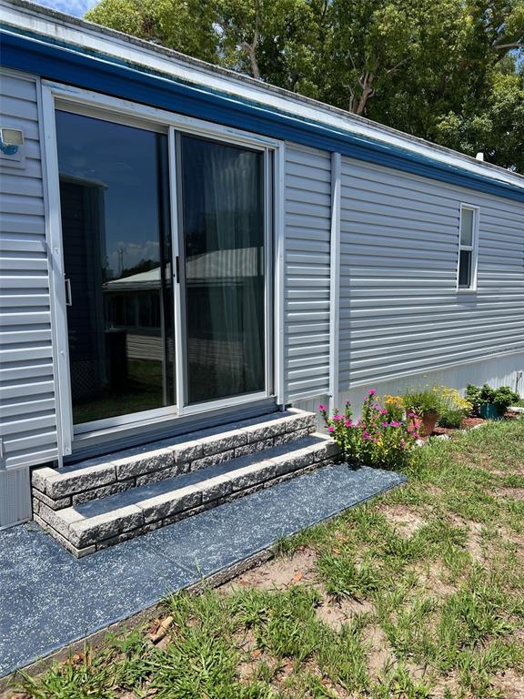 A gray mobile home exterior features a sliding glass door with stone steps and landscaping — 55 PALM FOREST DRIVE, LARGO, FL