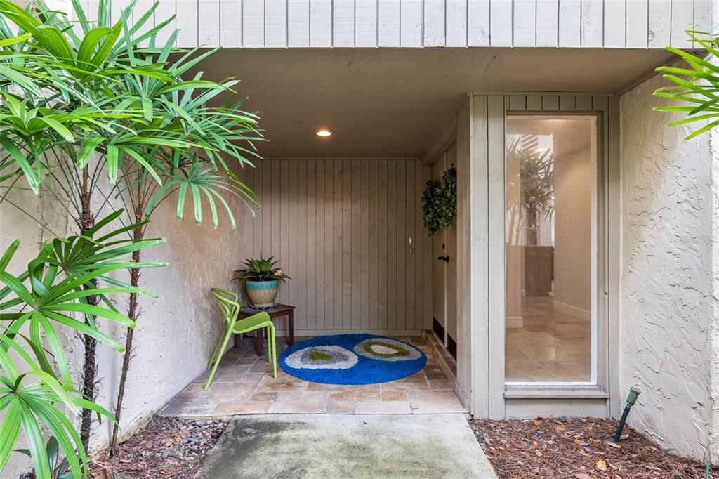 A covered entryway features a tiled floor, a green chair, a potted plant, and a rug — 117 RED CEDAR DRIVE, LONGWOOD, FL