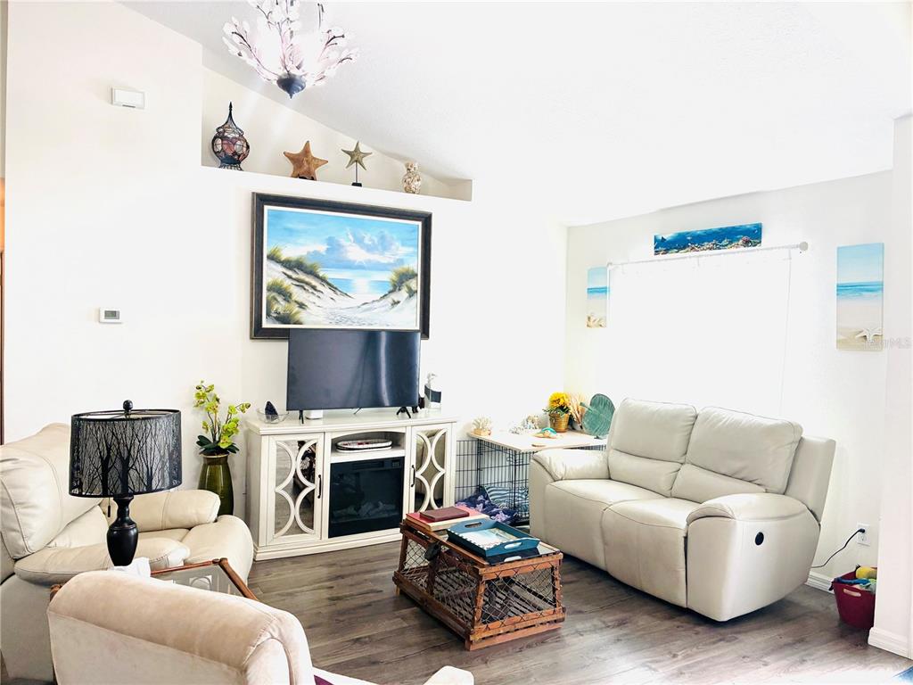 A living room features a white media console, a light-colored sofa, and a vaulted ceiling — 40551 E 5TH AVENUE, UMATILLA, FL