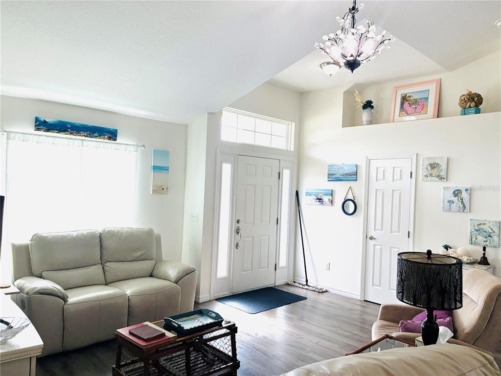 A living room features light-colored furniture, wood-look flooring, a vaulted ceiling, and a front entryway — 40551 E 5TH AVENUE, UMATILLA, FL