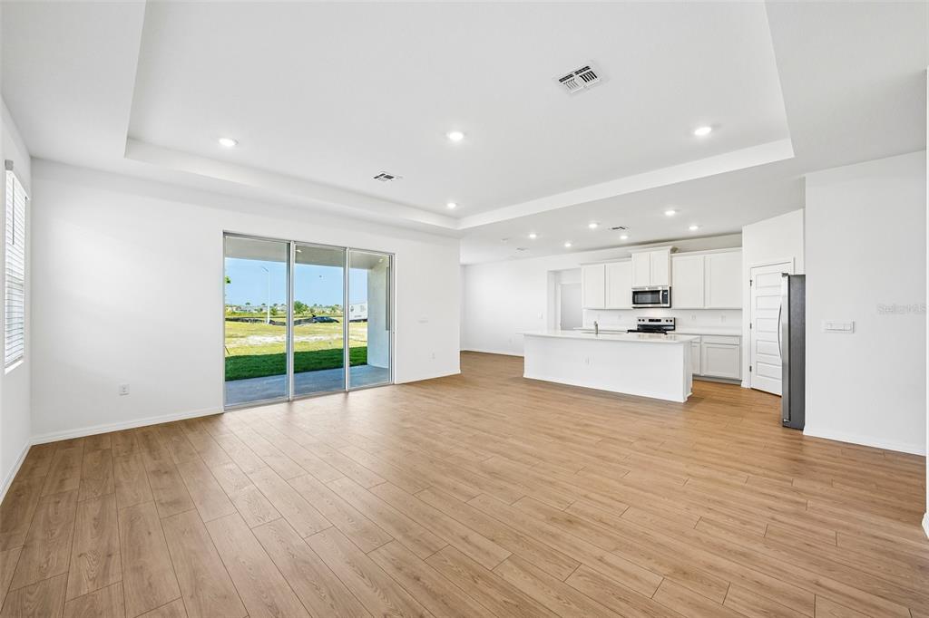 An open-concept living area features light wood-look flooring, a white kitchen, and sliding glass doors — 2265 HAMDEN WAY, MOUNT DORA, FL