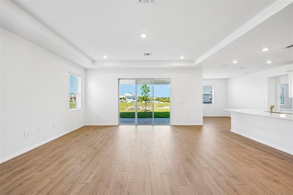An open-concept living area features light wood-look flooring, white walls, and sliding glass patio doors — 2265 HAMDEN WAY, MOUNT DORA, FL