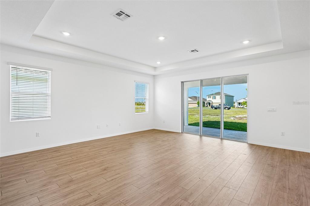 An empty living room features white walls, wood-look flooring, a tray ceiling, and sliding glass doors — 2265 HAMDEN WAY, MOUNT DORA, FL