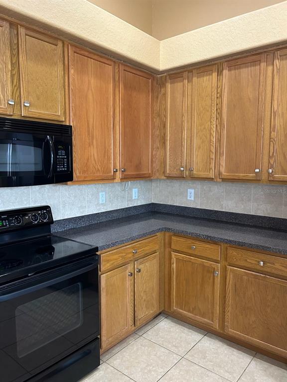 A kitchen features oak cabinets, black appliances, dark countertops, and light-colored tile flooring — 210 ROSANA DRIVE, BRANDON, FL