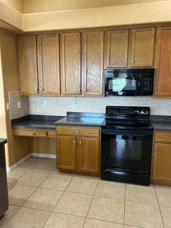 A kitchen features oak cabinets, black appliances, dark countertops, and light-colored tile flooring — 210 ROSANA DRIVE, BRANDON, FL