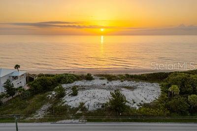 An aerial view shows a vacant, sandy beachfront lot at sunset next to a house — 6965 HIGHWAY A1A, MELBOURNE BEACH, FL