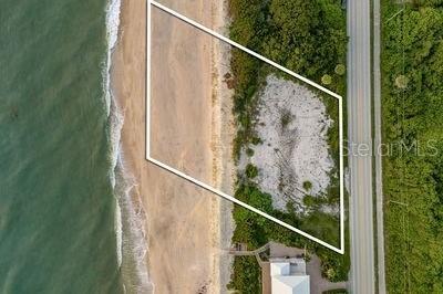 An aerial view shows a vacant, oceanfront lot outlined in white along a sandy beach — 6965 HIGHWAY A1A, MELBOURNE BEACH, FL
