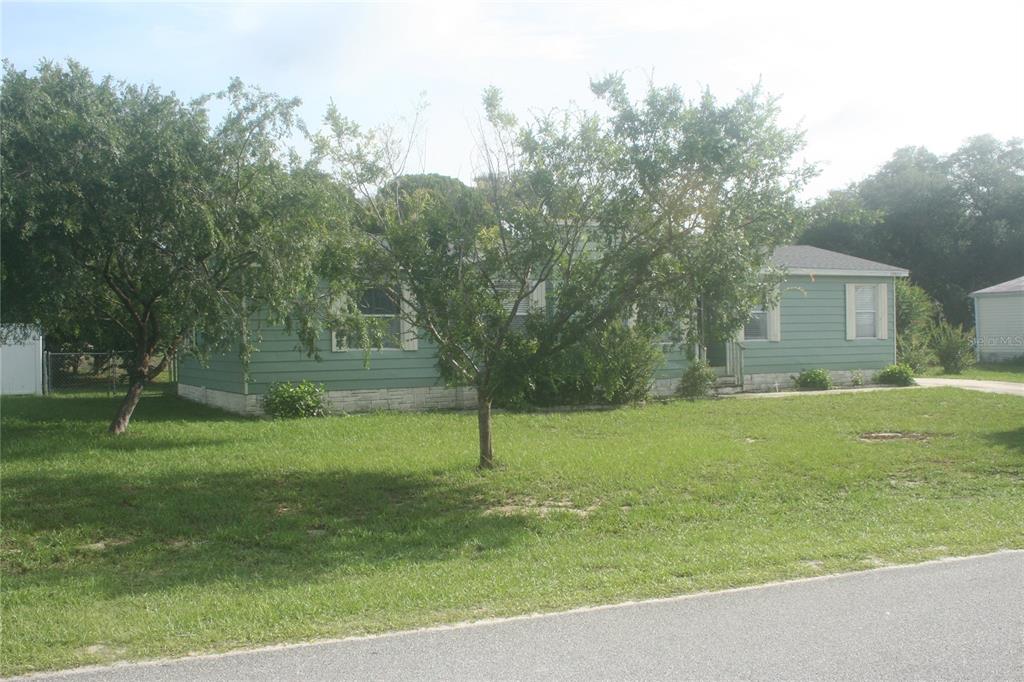 A single-story, light green house with a stone foundation sits behind trees on a lawn — 10035 SE 126TH LANE, BELLEVIEW, FL