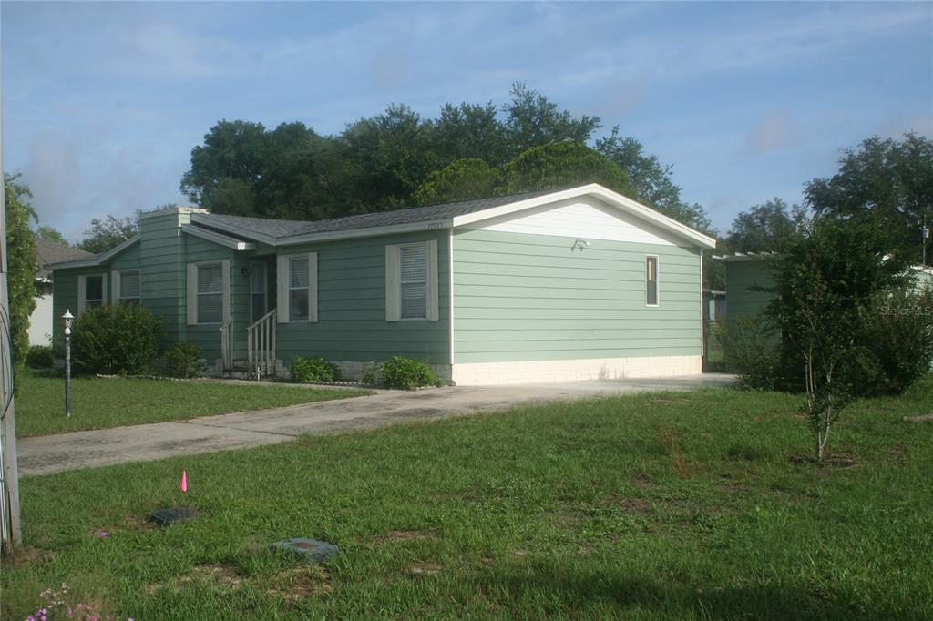 A light green single-story manufactured home with a concrete driveway and a white foundation — 10035 SE 126TH LANE, BELLEVIEW, FL