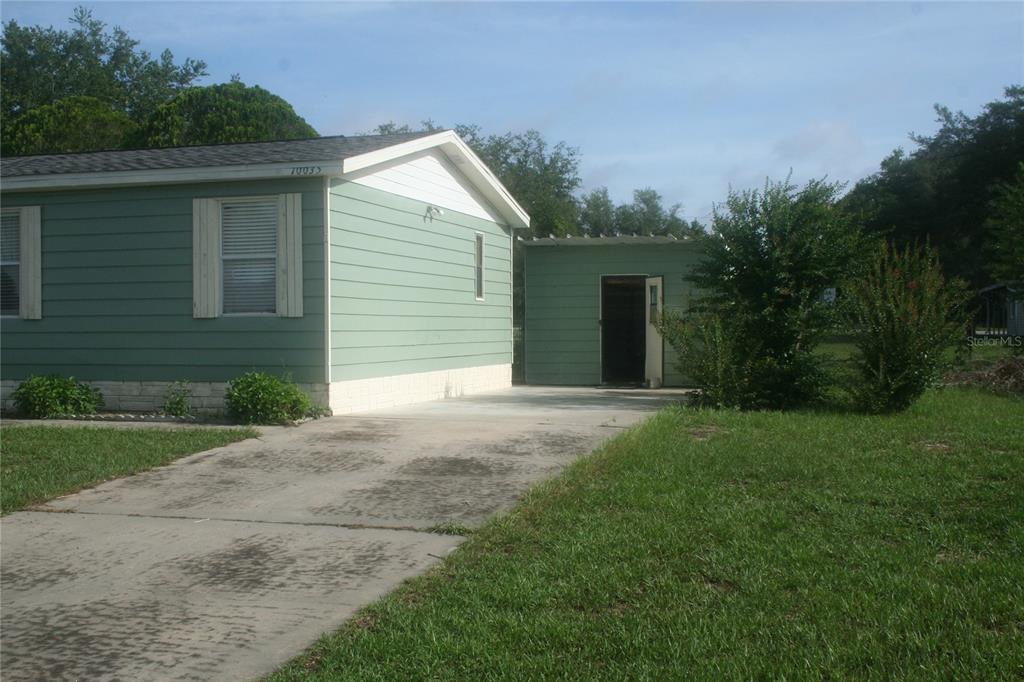 A light green manufactured home with a concrete driveway and an attached storage shed — 10035 SE 126TH LANE, BELLEVIEW, FL