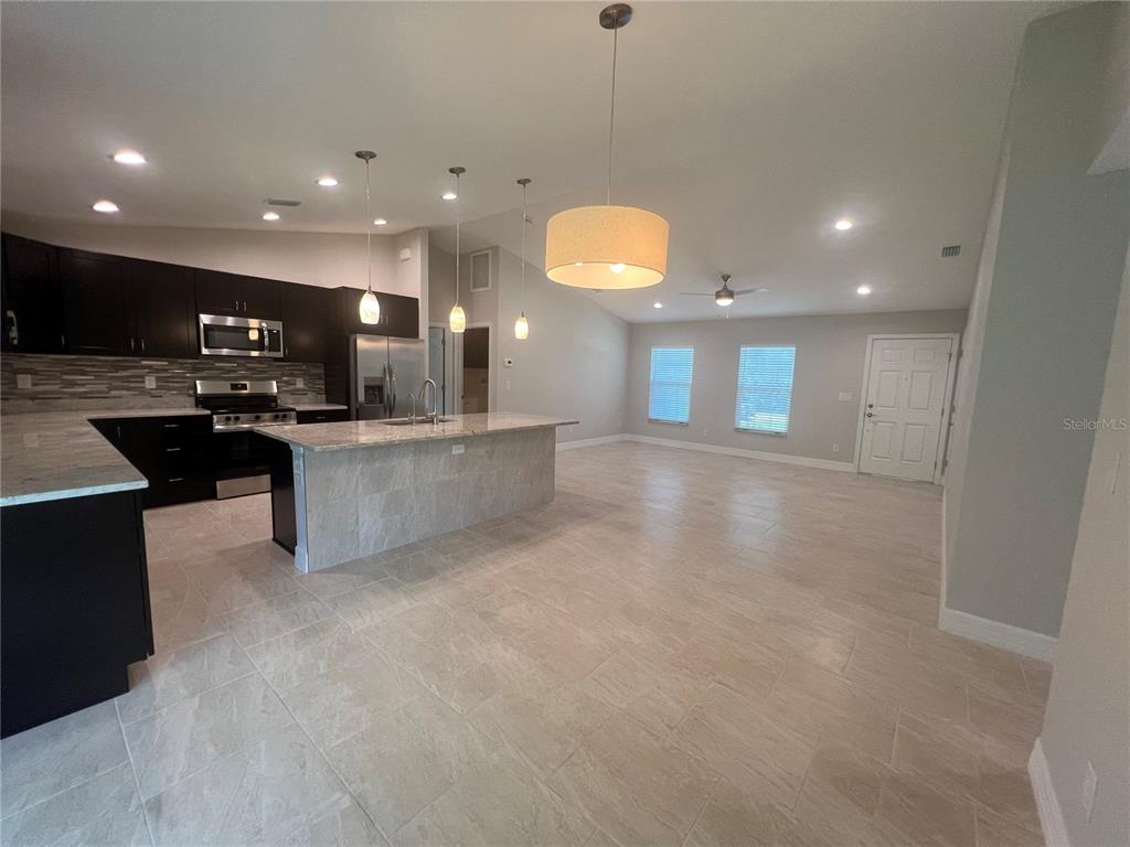 A kitchen with dark cabinets and a stone-topped island opens into a large living area — 4895 LAS ALMANOS AVENUE, NORTH PORT, FL