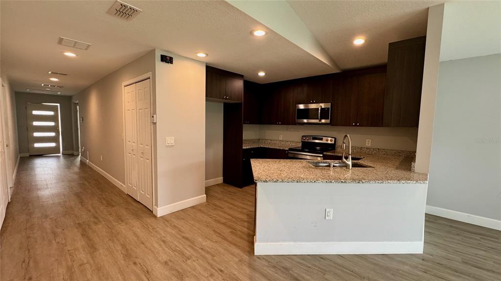 A kitchen with dark cabinets, granite countertops, and stainless steel appliances opens to a hallway — 5 N HART BOULEVARD, ORLANDO, FL