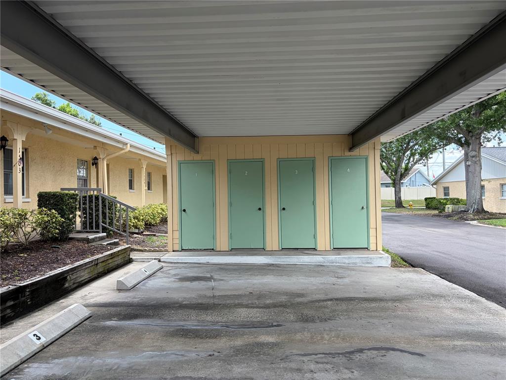 A covered carport features four numbered green storage unit doors facing a concrete parking area — 2465 NORTHSIDE DRIVE UNIT 1502, CLEARWATER, FL