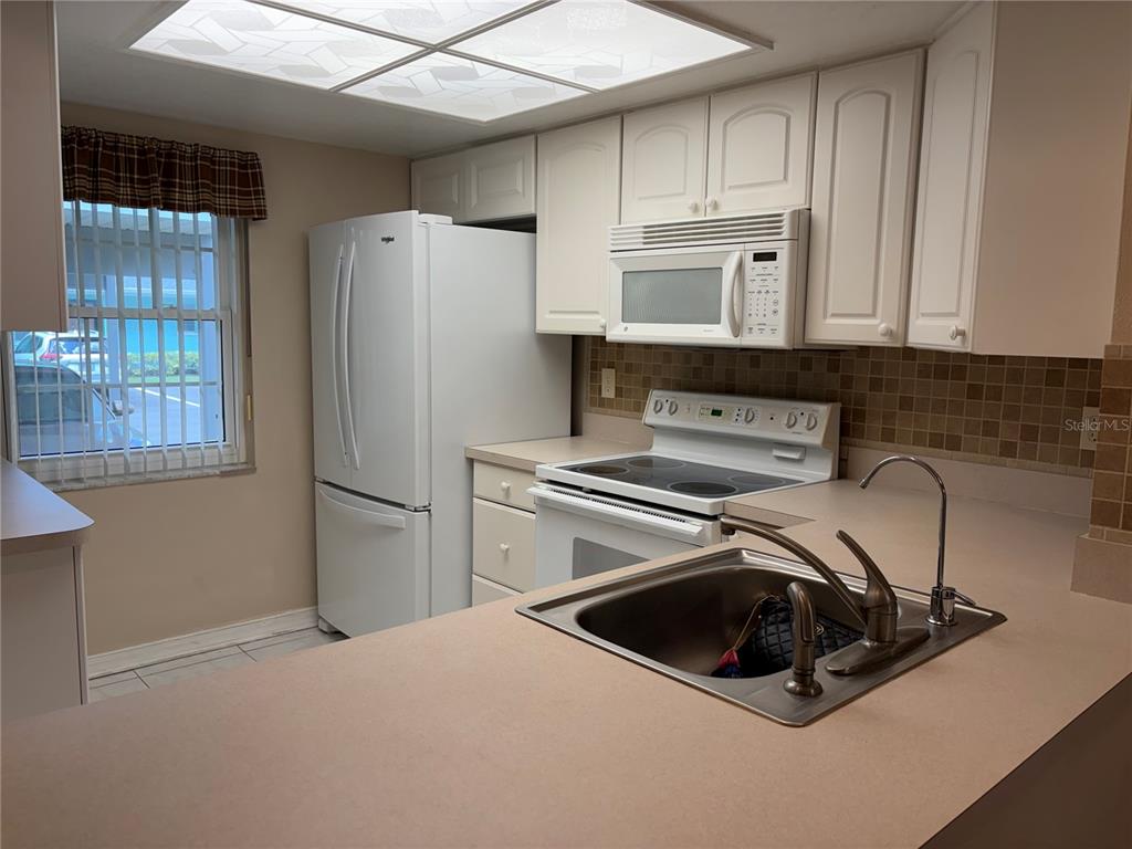 A kitchen features white cabinetry, a stainless steel sink, and a window with vertical blinds — 2465 NORTHSIDE DRIVE UNIT 1502, CLEARWATER, FL