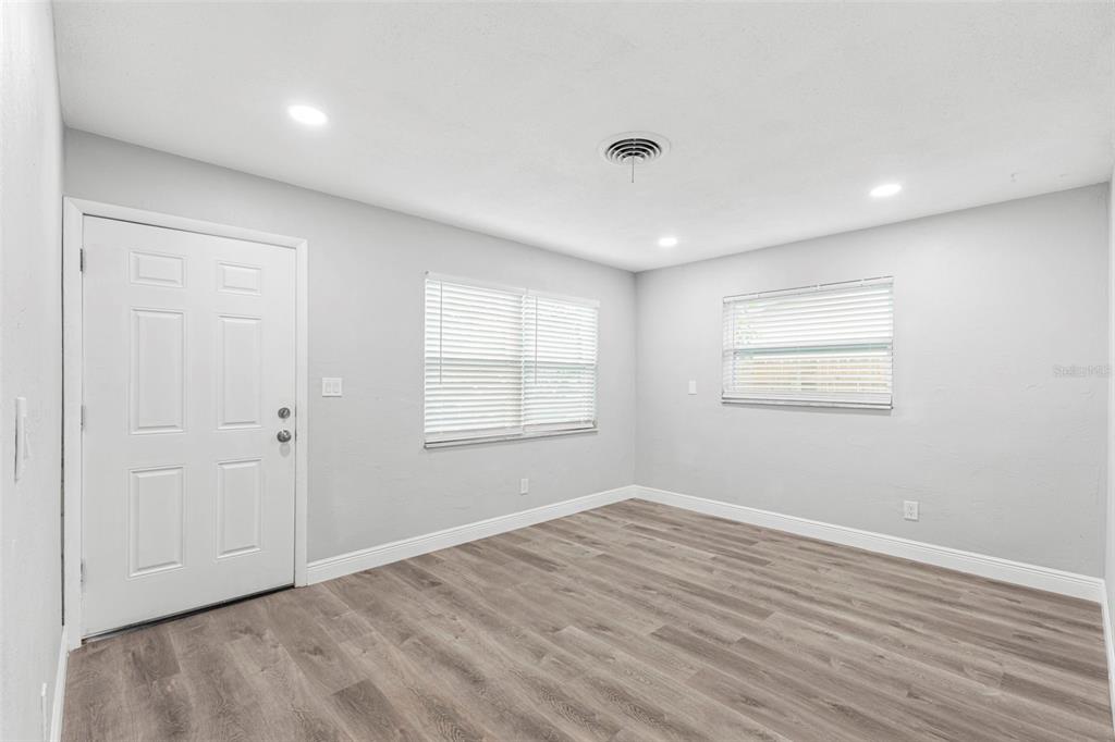 An empty room with light gray walls, wood-look flooring, two windows with blinds, and a door — 2443 26TH AVENUE S, ST PETERSBURG, FL