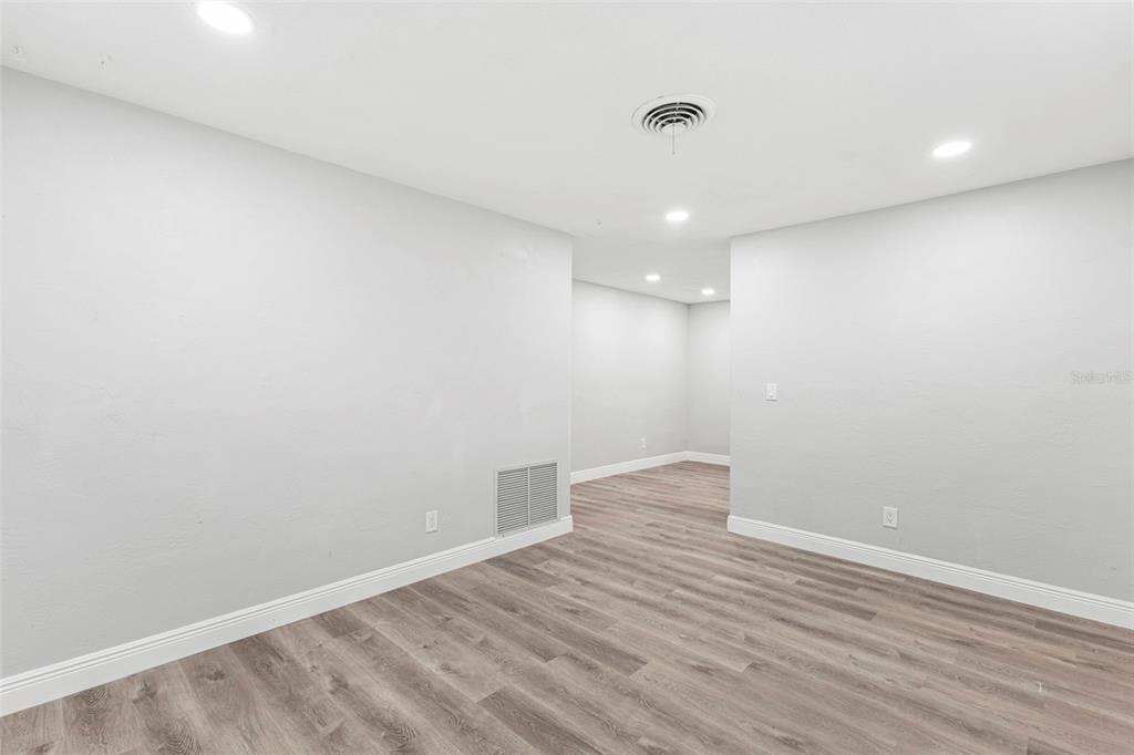 An empty room features light gray walls, wood-look flooring, recessed lighting, and a floor vent — 2443 26TH AVENUE S, ST PETERSBURG, FL