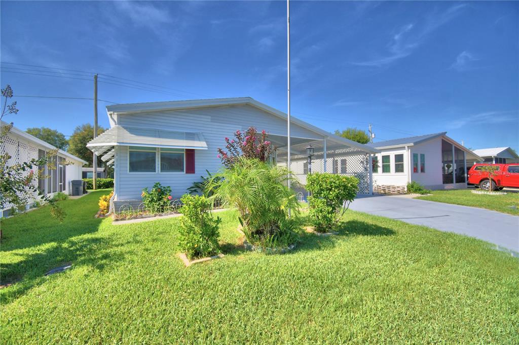 A light blue manufactured home with a concrete driveway, carport, and landscaped front yard — 6086 SOUTHERN OAKS DRIVE, WINTER HAVEN, FL