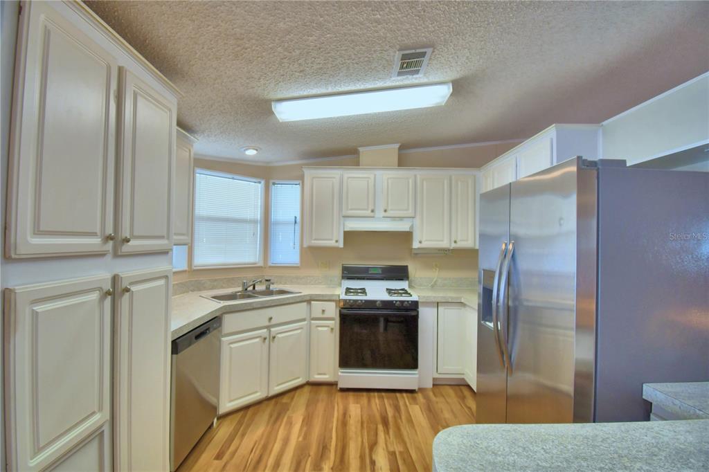 A kitchen features white cabinets, a breakfast bar, stainless steel appliances, and wood-look flooring — 6086 SOUTHERN OAKS DRIVE, WINTER HAVEN, FL