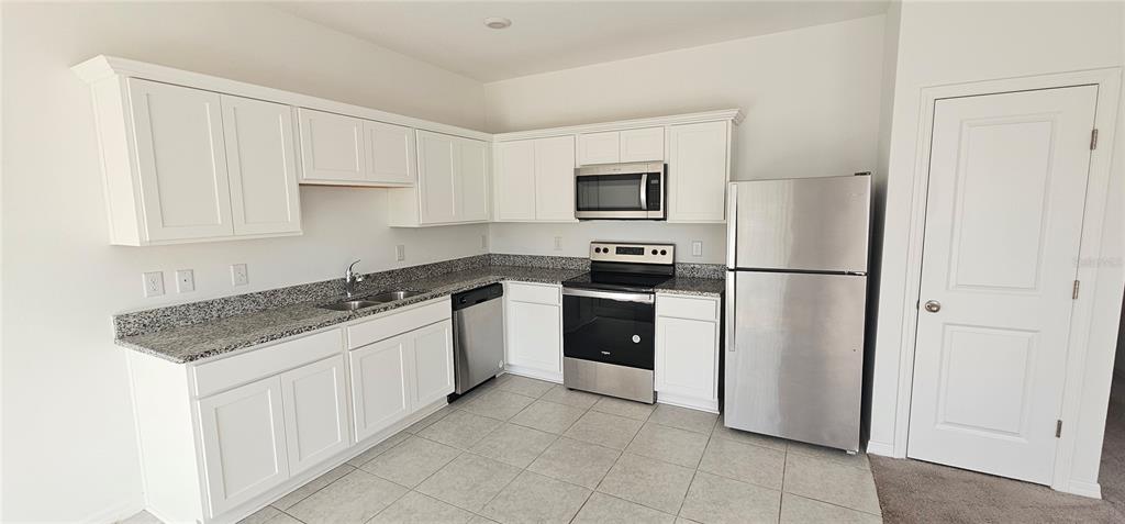 A kitchen features white cabinets, granite countertops, stainless steel appliances, and light-colored tile flooring — 1045 APPLETON STREET, DAVENPORT, FL