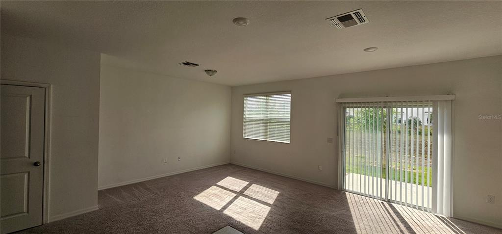 An empty living room features beige carpeting, white walls, a sliding glass door, and a window — 1045 APPLETON STREET, DAVENPORT, FL