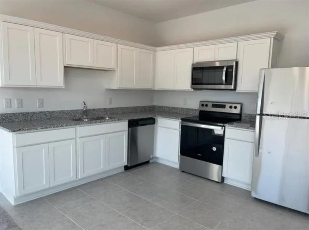 A kitchen with white cabinets, granite countertops, stainless steel appliances, and light-colored tile flooring — 1045 APPLETON STREET, DAVENPORT, FL