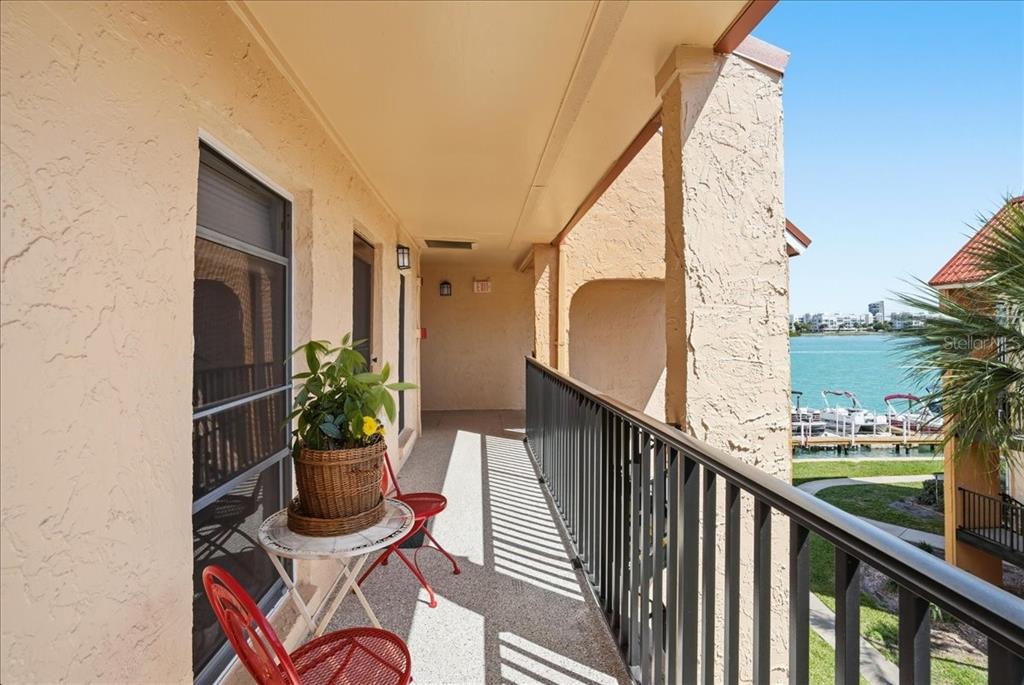 A covered balcony with red chairs and a small table overlooks a waterfront marina — 8931 BLIND PASS ROAD UNIT 360, ST PETE BEACH, FL