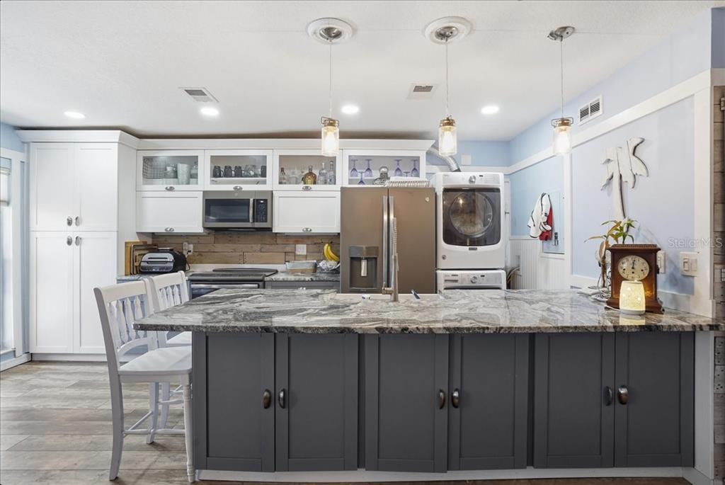 A kitchen features a dark gray island, white cabinetry, granite countertops, and a stacked laundry unit — 8931 BLIND PASS ROAD UNIT 360, ST PETE BEACH, FL
