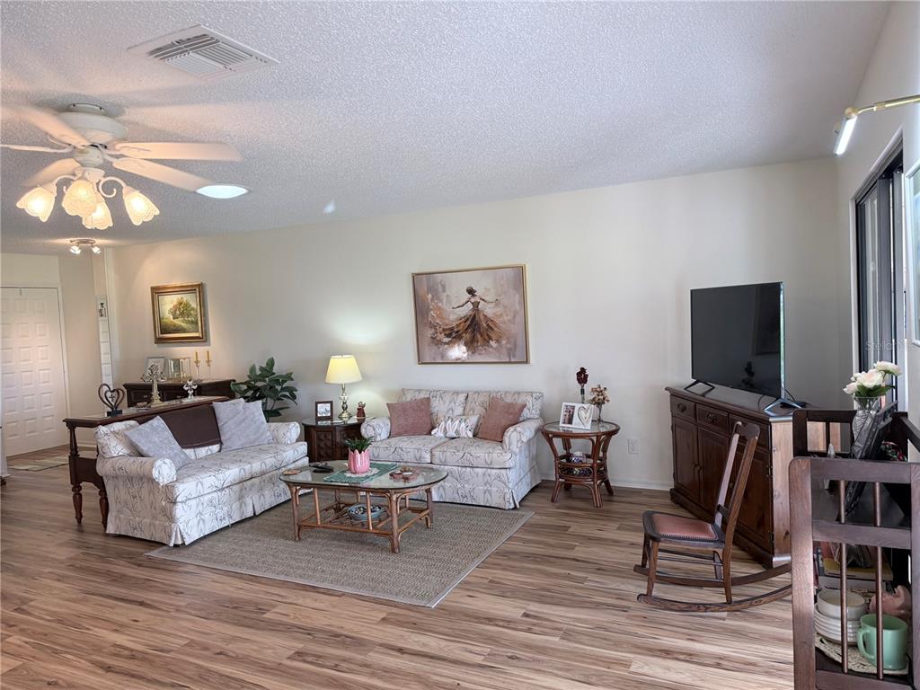 A living room features light wood-look flooring, two patterned sofas, a television, and a ceiling fan — 2417 LOCKSLEY STREET UNIT 229, SUN CITY CENTER, FL