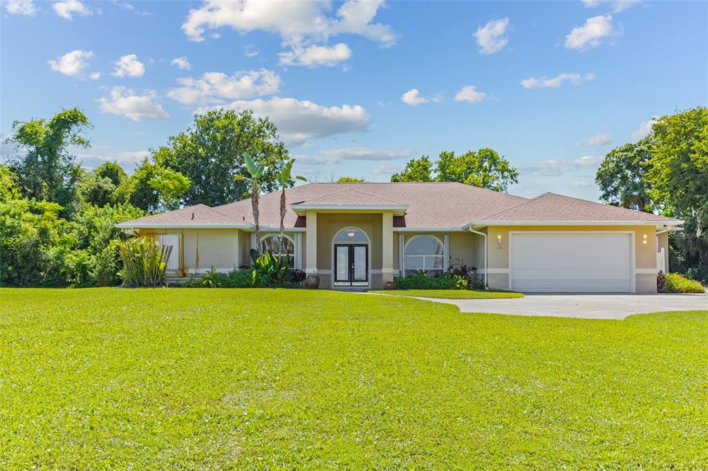 A single-story house with a tan stucco exterior, a two-car garage, and a large lawn — 4135 INDIAN RIVER DRIVE, COCOA, FL