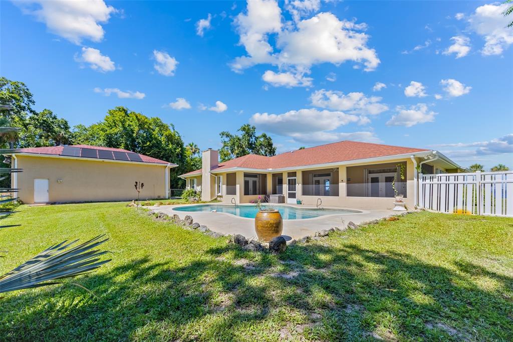 A backyard features a swimming pool, a tan house with a red roof, and landscaping — 4135 INDIAN RIVER DRIVE, COCOA, FL