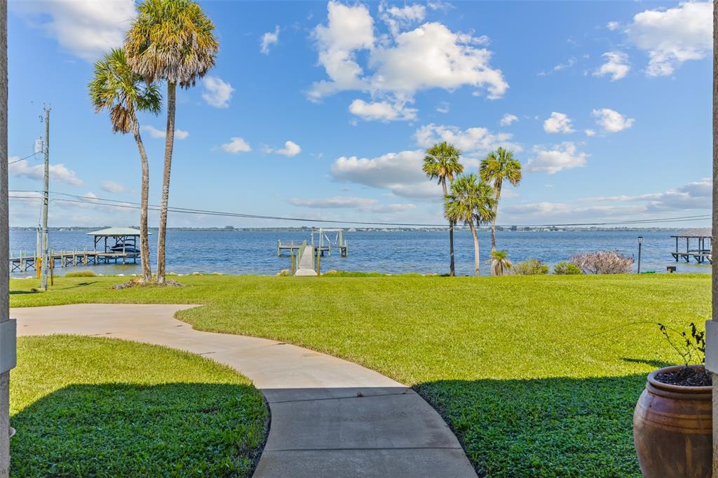 A concrete walkway leads across a grassy lawn toward a dock on a large lake — 4135 INDIAN RIVER DRIVE, COCOA, FL