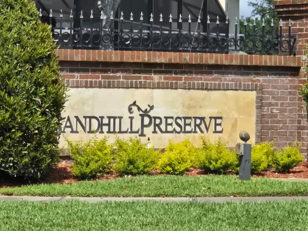 A brick wall with a sign reading Sandhill Preserve sits behind a row of green bushes — 2415 SAND ARBOR CIRCLE, ORLANDO, FL