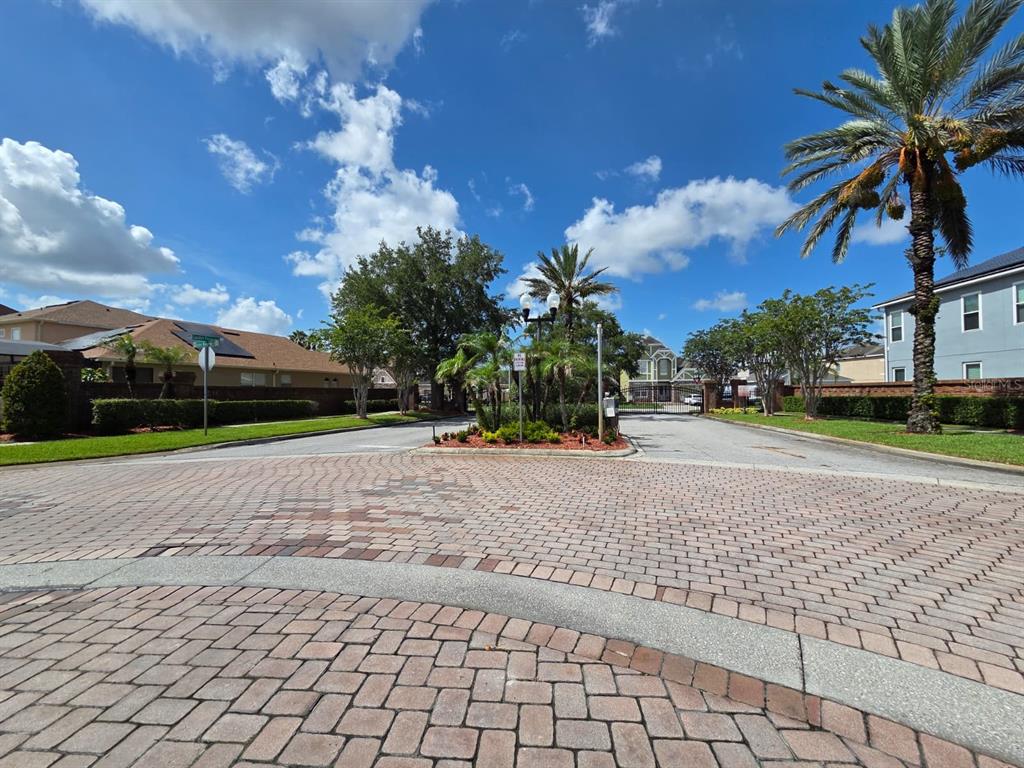 A gated entrance with a brick-paved driveway, palm trees, and surrounding residential homes — 2415 SAND ARBOR CIRCLE, ORLANDO, FL