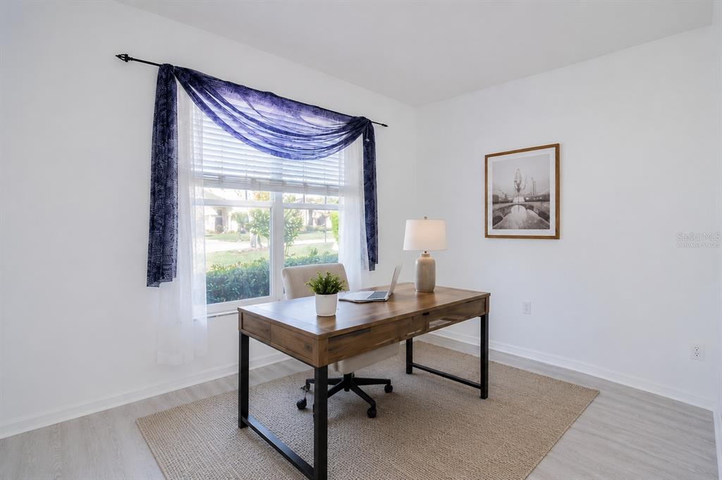 A home office features a wooden desk, a rolling chair, and a window with blue curtains — 4810 WATER LARK WAY, VALRICO, FL