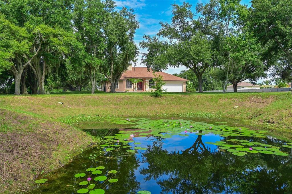 A house with a garage sits behind a pond filled with lily pads and trees — 4415 N RYE ROAD, PARRISH, FL