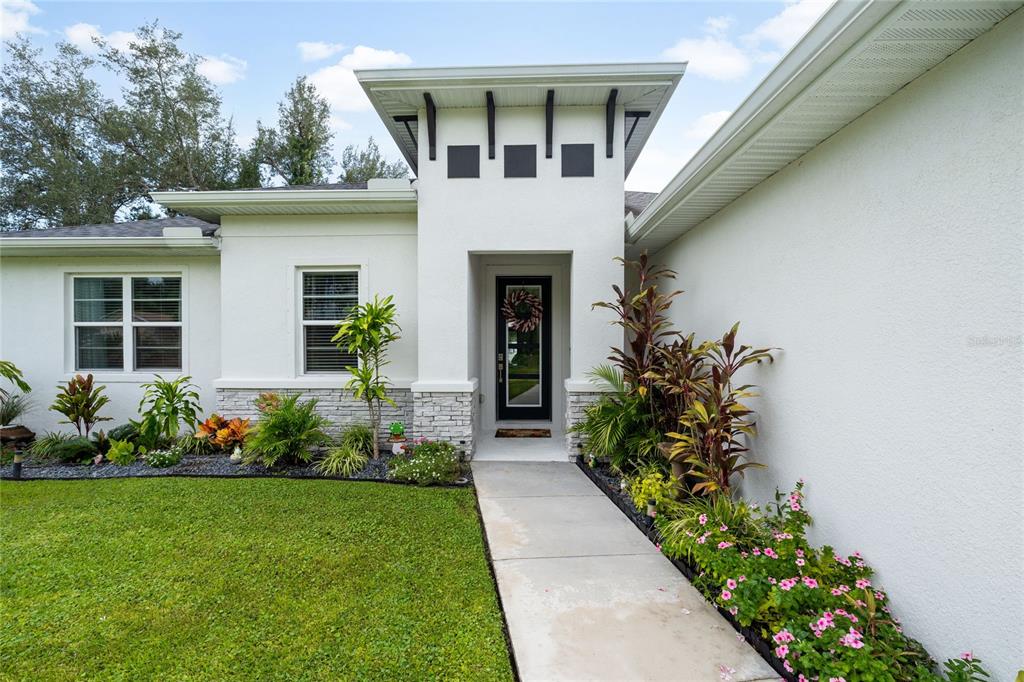 A white house exterior features a central entryway with a flat roof and stone accents — 4033 UNION LANE, NORTH PORT, FL