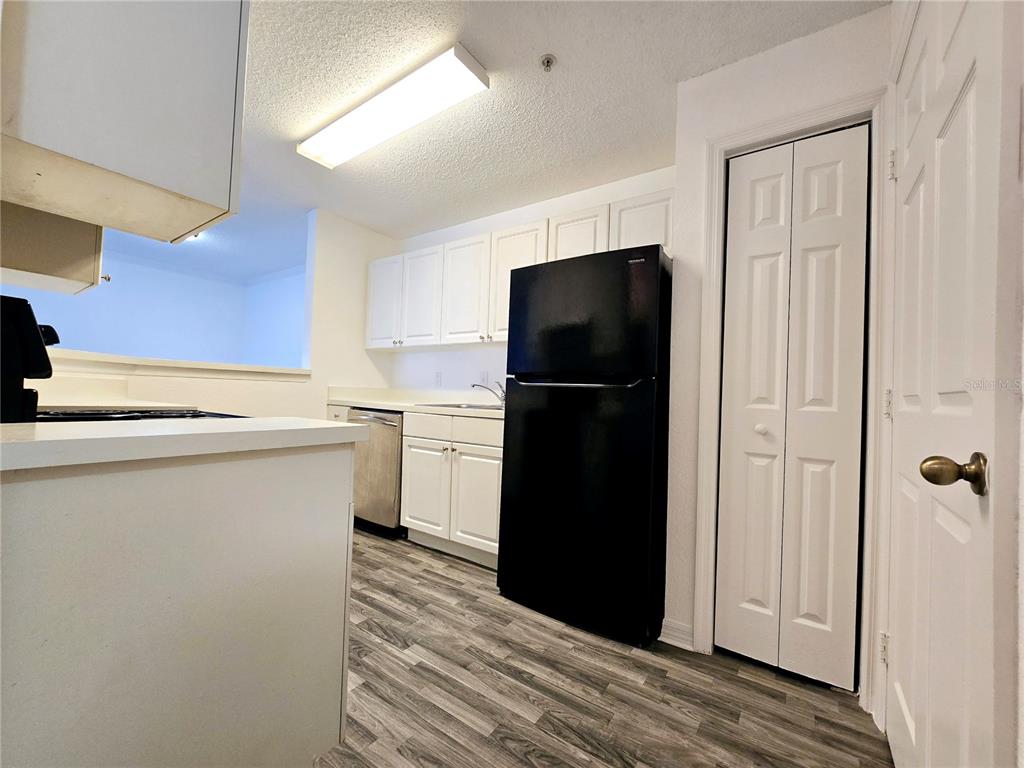 A kitchen features white cabinets, a black refrigerator, stainless steel dishwasher, and wood-look flooring — 18001 RICHMOND PLACE DRIVE UNIT 132, TAMPA, FL
