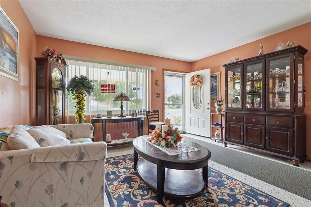 A living room with orange walls, a floral sofa, a coffee table, and a china cabinet — 6832 OSWEGO DRIVE, MOUNT DORA, FL