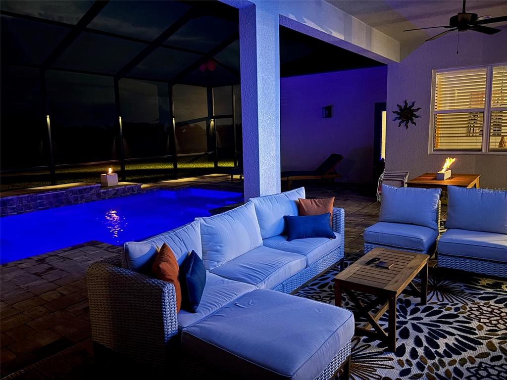 A covered patio at night features a sectional sofa, a coffee table, and a swimming pool — 7074 BENTRIDGE DR, LAKELAND, FL