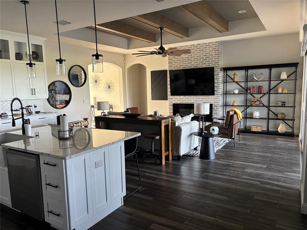 An open-concept kitchen and living area features white cabinetry, a brick fireplace, and wood beams — 7074 BENTRIDGE DR, LAKELAND, FL