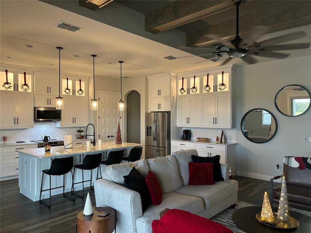 A modern open-concept kitchen and living area features white cabinetry, a marble island, and sofas — 7074 BENTRIDGE DR, LAKELAND, FL