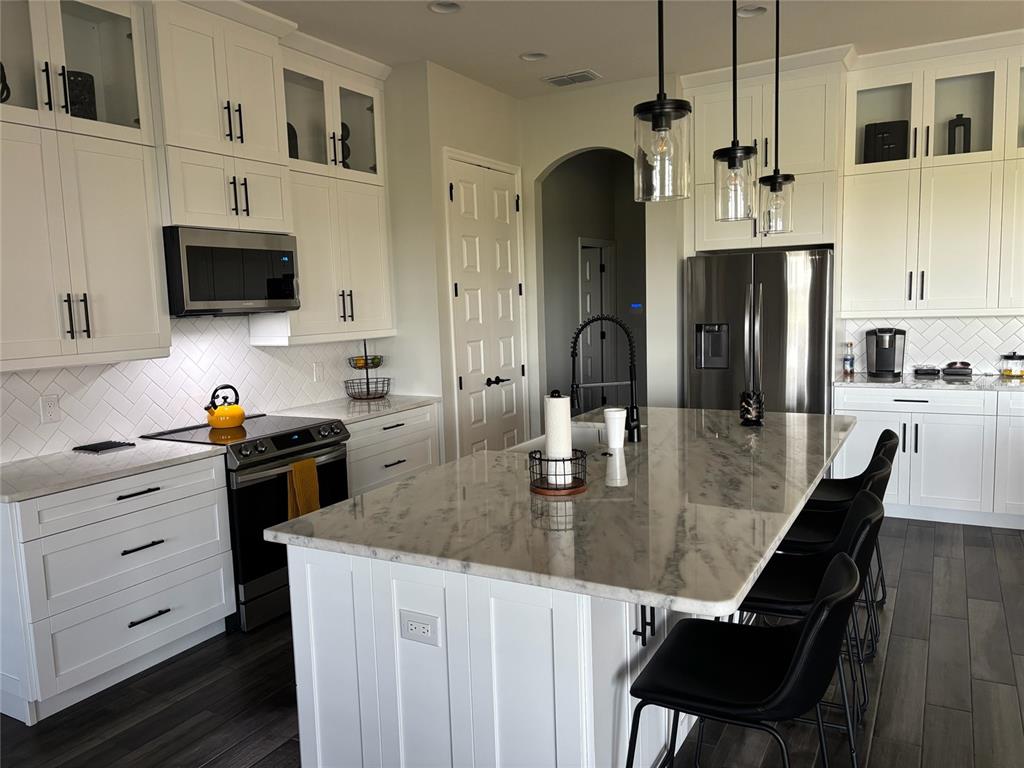 A modern kitchen features white cabinetry, a marble-topped island, stainless steel appliances, and dark flooring — 7074 BENTRIDGE DR, LAKELAND, FL