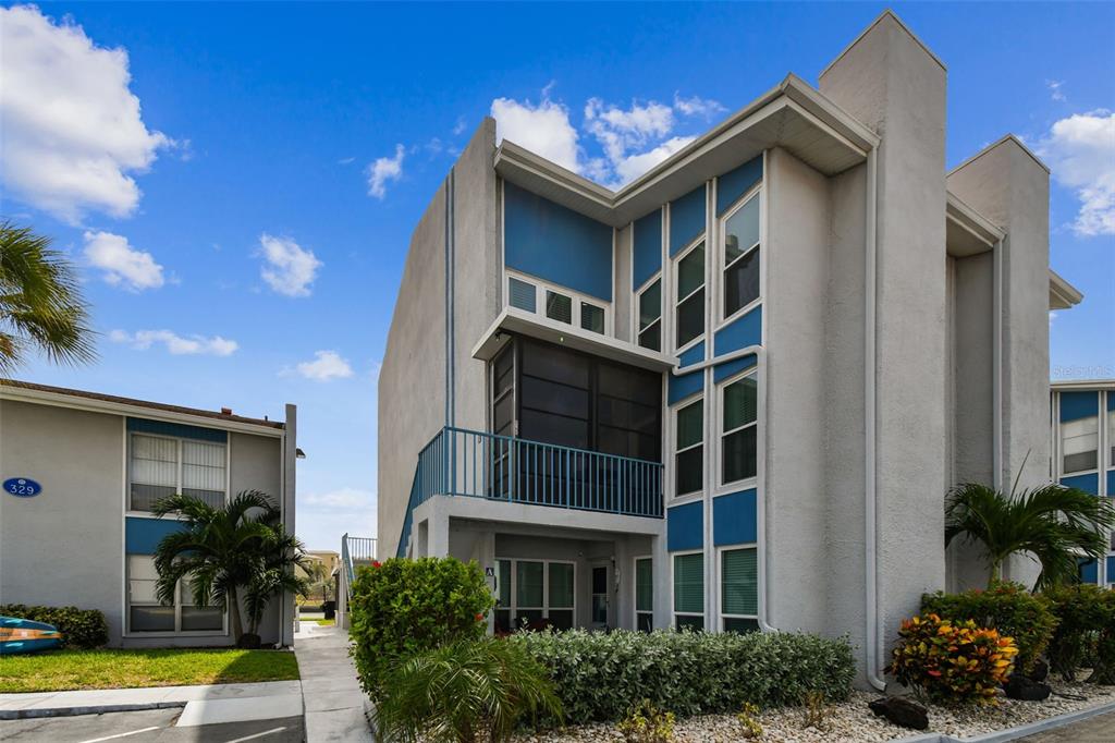 Exterior view of a multi-story apartment building with blue accents and a screened-in balcony — 315 MEDALLION BOULEVARD UNIT E, MADEIRA BEACH, FL
