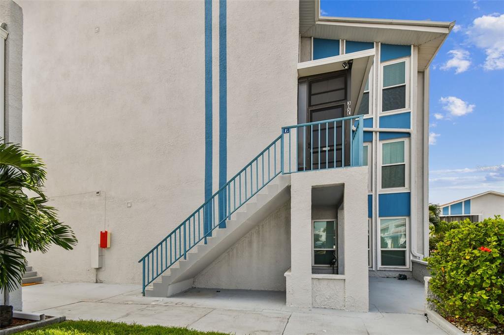 An exterior view of a multi-story building with blue accents, a staircase, and a balcony — 315 MEDALLION BOULEVARD UNIT E, MADEIRA BEACH, FL