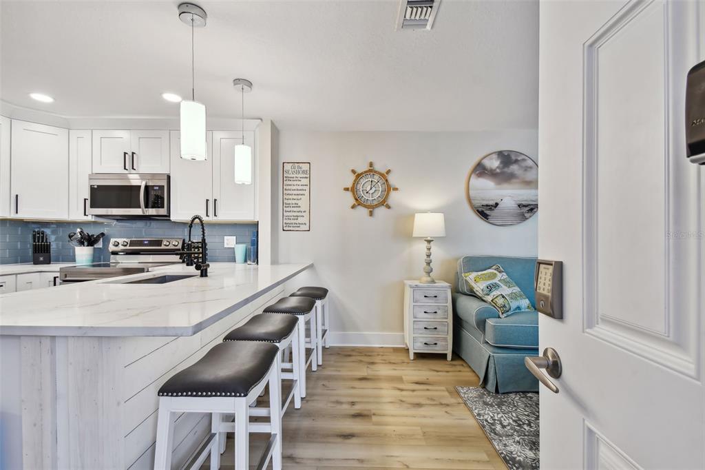 A kitchen with white cabinets and a breakfast bar overlooks a small coastal-themed seating area — 315 MEDALLION BOULEVARD UNIT E, MADEIRA BEACH, FL