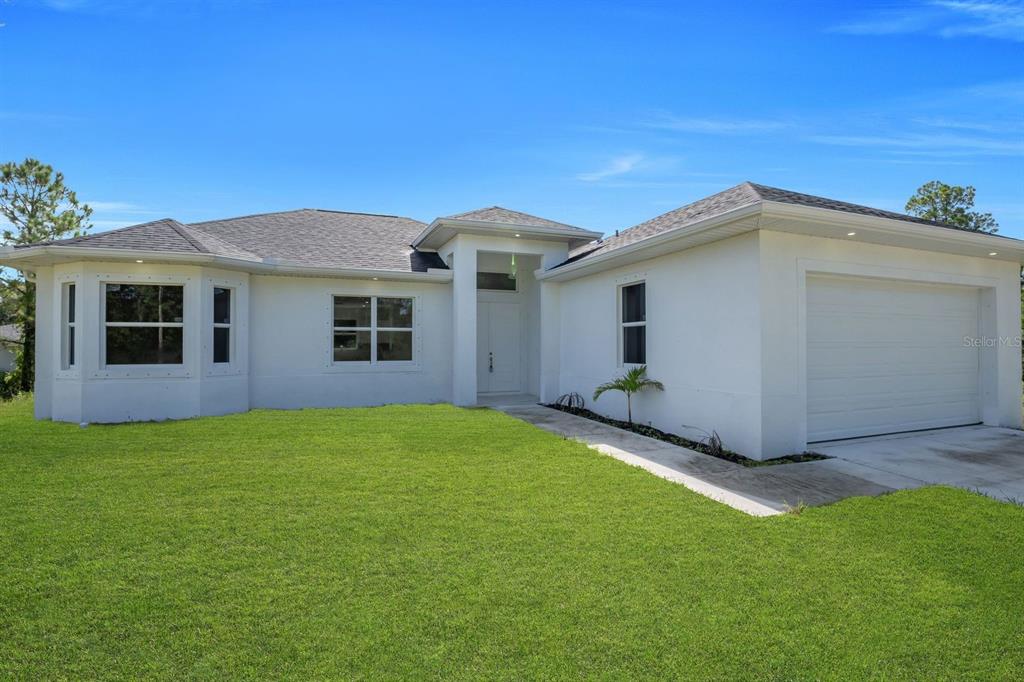 A single-story white house with a garage and a bay window under a blue sky — 523 HARRY THAYER AVENUE S, LEHIGH ACRES, FL