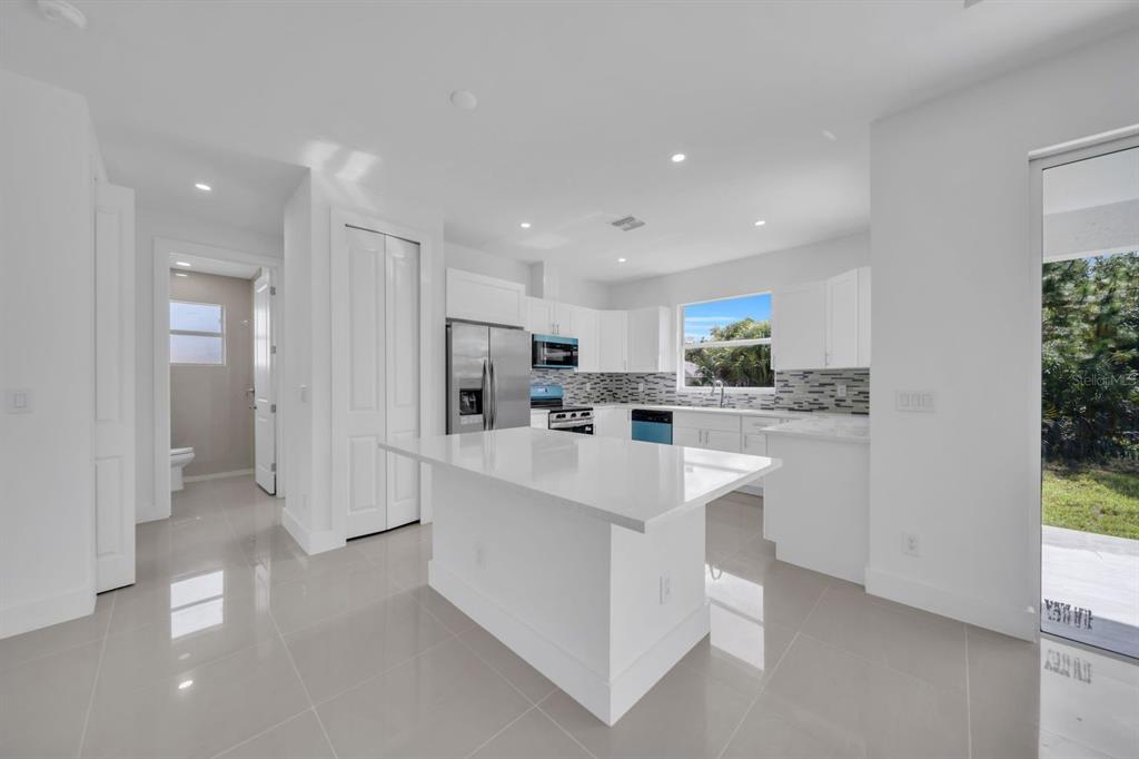 A modern kitchen features white cabinetry, a central island with a quartz countertop, and tile flooring — 523 HARRY THAYER AVENUE S, LEHIGH ACRES, FL