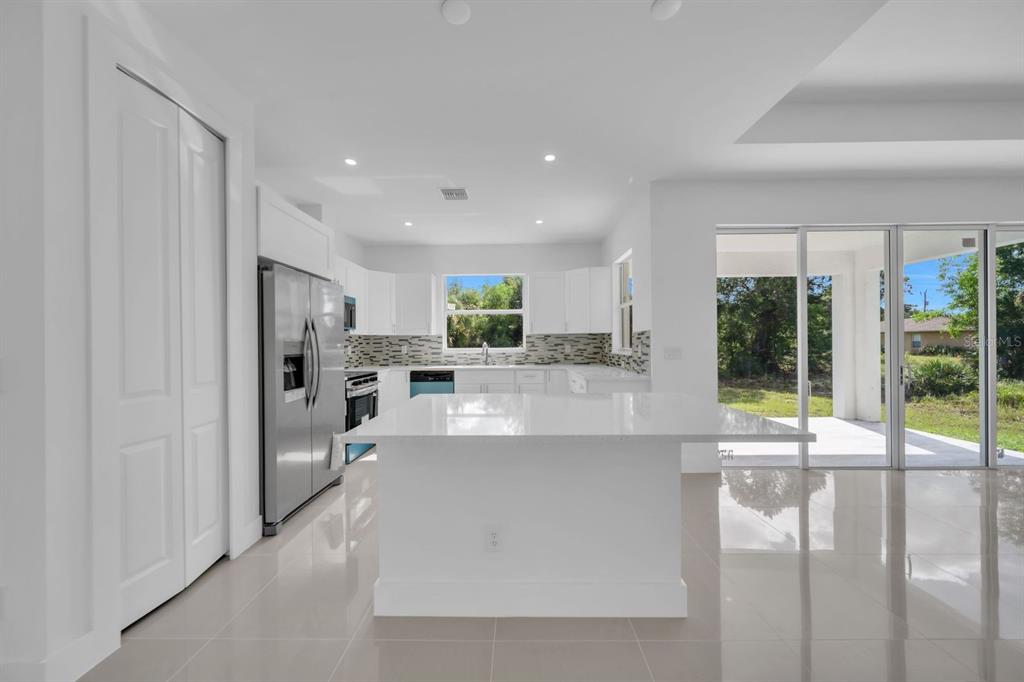 A modern kitchen features white cabinetry, stainless steel appliances, a central island, and sliding doors — 523 HARRY THAYER AVENUE S, LEHIGH ACRES, FL